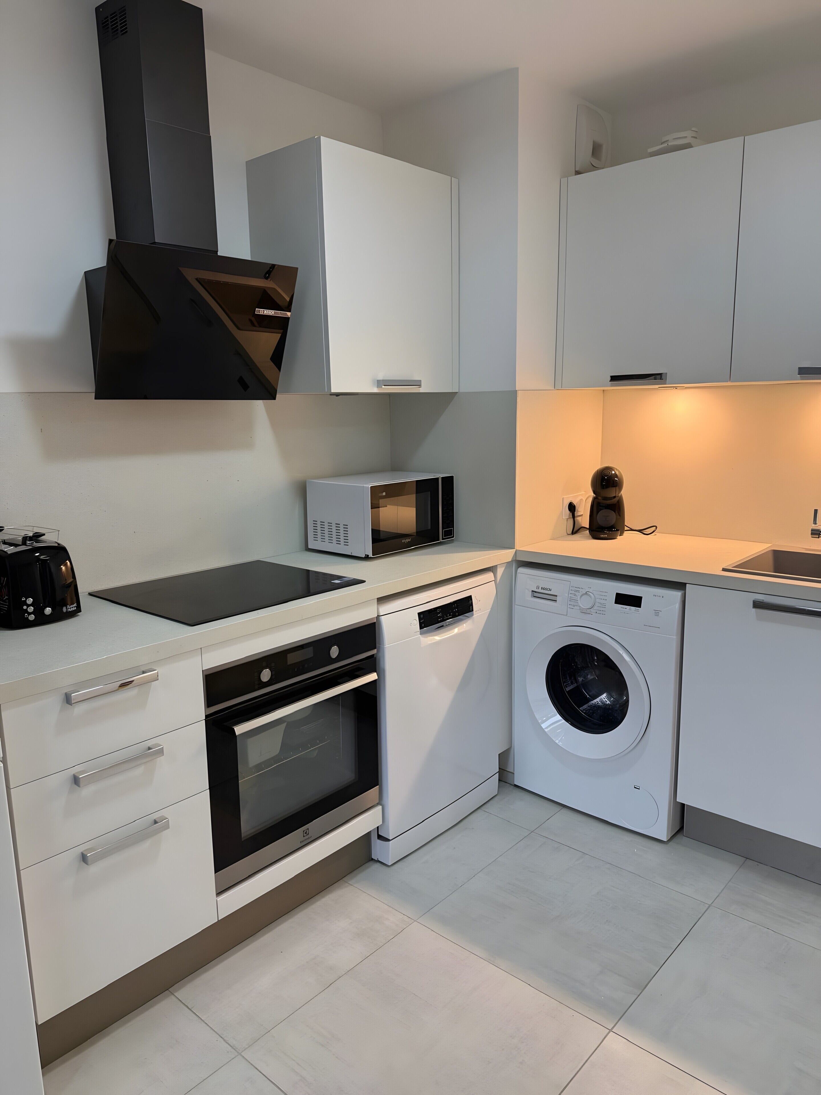 Cocina moderna con armarios blancos, horno empotrado, microondas, lavavajillas y lavadora.