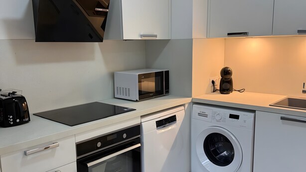 A modern kitchen with white cabinetry, a built-in oven, microwave, dishwasher, and washing machine.