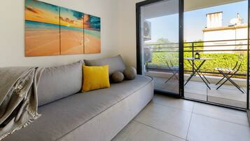 Een moderne woonkamer met een grijze bank, een geel kussen en een groot schilderij van een strand.