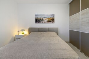 Ein Schlafzimmer mit einem Bett, einem Nachttisch mit Lampe und einem Bild von einer Strandlandschaft.