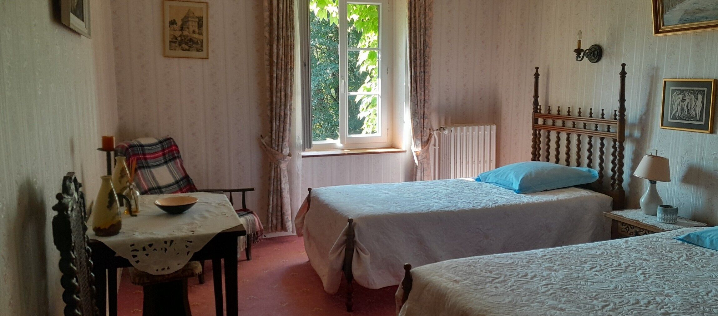 Une pièce avec deux lits, une table avec un bol, une chaise, une fenêtre avec des rideaux et un radiateur.