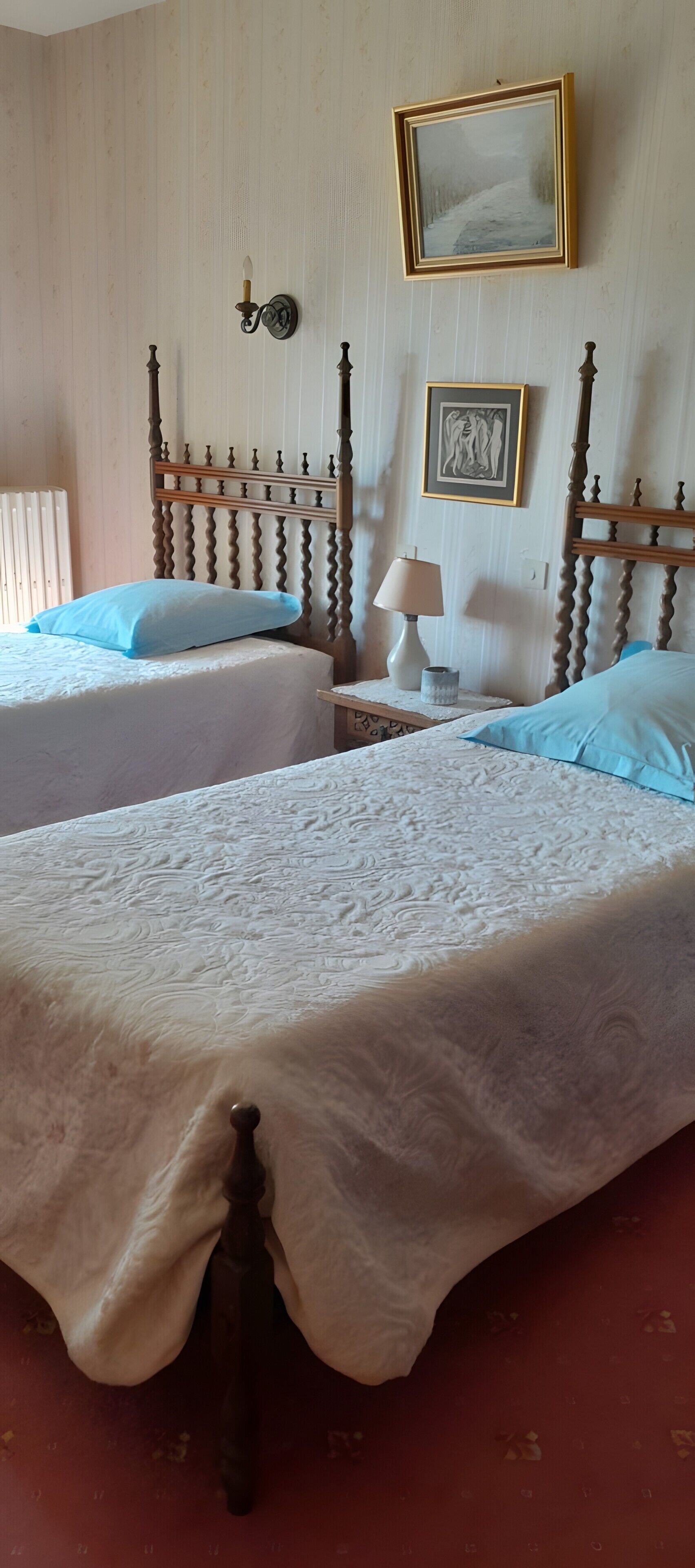 Une chambre avec deux lits, une table de chevet, une lampe et un luminaire fixé au mur.