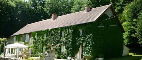 Une maison avec un toit en pente, entourée d’une végétation luxuriante et d’une pelouse bien entretenue.
