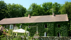 Uma casa com telhado de telhas, parede de pedra e um jardim com um guarda-sol branco.