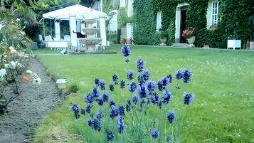 Een tuin met een fontein, een tuinhuisje en een huis dat deels met klimop is begroeid.