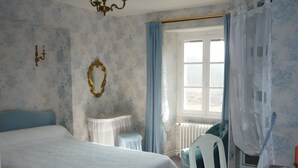 A bedroom with a large bed, a bedside table, a chair, a window with curtains, and a wall-mounted mirror.