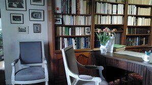 A room with two white chairs, a wooden desk, a bookshelf filled with books, and a patterned carpet.