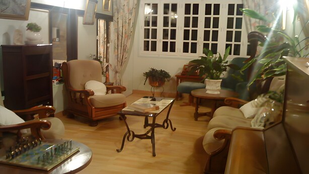 A cozy living room with a wooden coffee table, a comfortable armchair, a sofa, and a dining table.