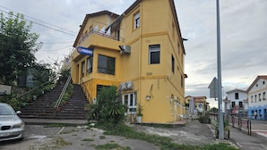 A yellow building with a blue sign, a staircase, and a car parked in front.