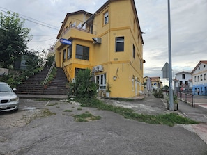 A yellow building with a blue sign, a staircase, and a car parked in front. - APARTAMENTOS Y ESTUDIOS EL CENTRO (vargas)