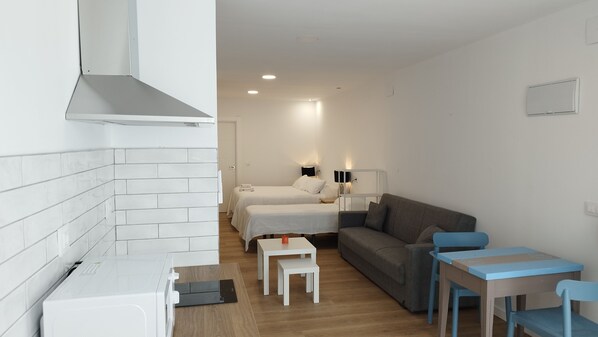 A compact hotel room with a kitchenette, two beds, a sofa, and a small table with chairs. - APARTAMENTOS Y ESTUDIOS EL CENTRO (vargas)