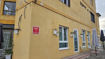 Un immeuble jaune avec une enseigne rouge indiquant la présence d’appartements destinés aux touristes. On y trouve des tables et des chaises à l’extérieur, ainsi que des plantes en pot sur les rebords de fenêtres.