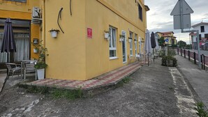 A yellow building with outdoor seating, a red sign, and a triangular warning sign.