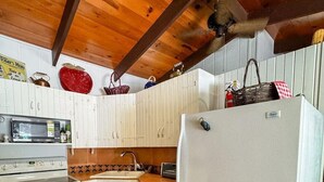 Une cuisine avec des meubles blancs, un four à micro-ondes, une cuisinière, un réfrigérateur et un plafond en bois.