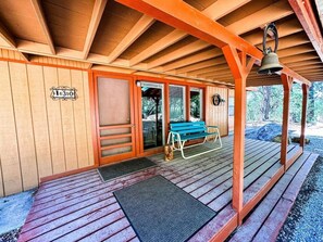 Uma cabana de madeira com varanda, um banco e um sino.