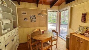 Un coin repas chaleureux avec une table et des chaises en bois, un luminaire suspendu et une vue sur l’extérieur grâce à une porte vitrée.