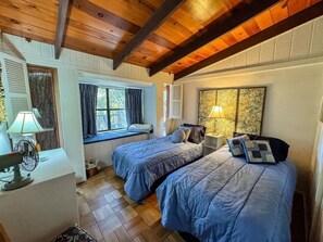 Een kamer met twee bedden, een vensterbank en een ventilator.