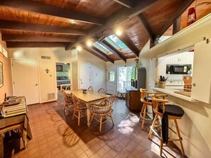 Un coin repas avec une table et des chaises en bois, une cuisine équipée d’un four à micro-ondes et un plafond avec des poutres apparentes.