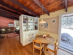 A cozy living room with a wooden ceiling, a dining area with a round table and chairs, and a kitchen with white cabinets and shelves. - Tranquil Pines Retreat (High Rolls)