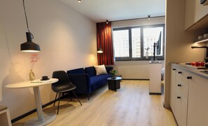 A modern living space with a sofa, a dining table, a small side table, and a kitchen area with a sink and countertop. - Ipartment Frankfurt Eastside @Home By Best Western (Frankfurt)