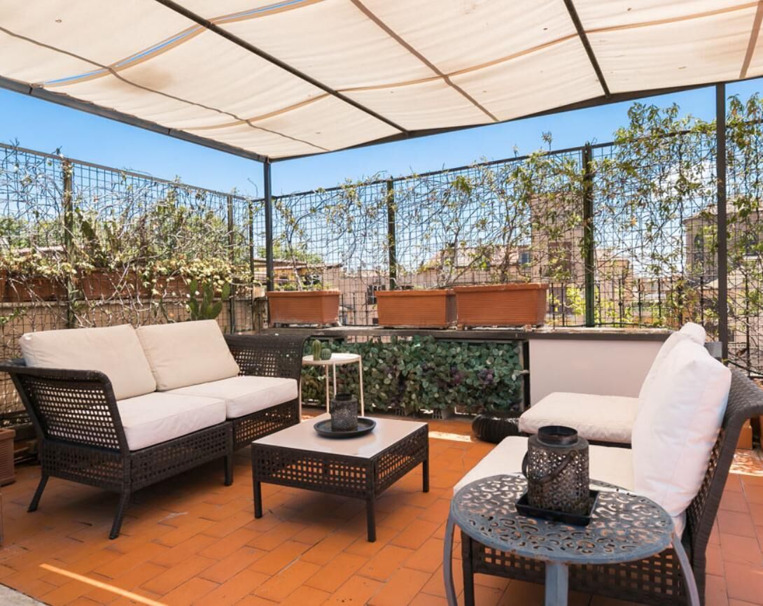 An outdoor patio with a covered seating area, including a sofa and chairs, a table, and decorative vases.