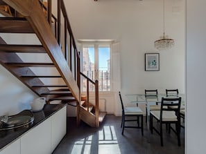 A modern interior with a wooden staircase, a dining area with glass tables, and a view through an open door. - Penthouse in Trastevere (Roma)