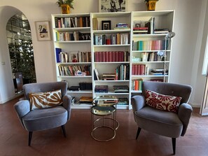 A living room with two grey armchairs, a small glass table, and a large bookshelf filled with books. - Penthouse in Trastevere (Roma)