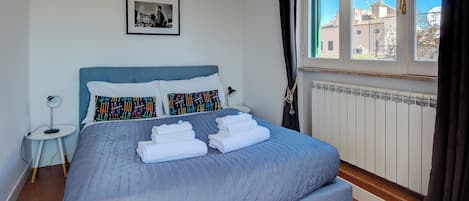 Un dormitorio con cama, mesita de noche, radiador y ventana con cortinas.