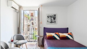 A bedroom with a bed, a chair, a small table, and an air conditioning unit.