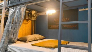 Una cama litera con cabecera, un ventilador fijado a la pared y una cama con una colcha amarilla.