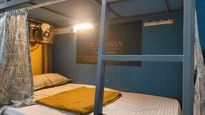 Een slaapkamer met stapelbed, een ventilator, een kussen en een bordje aan de muur.