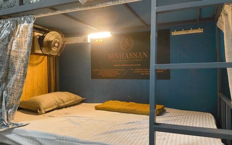 A bunk bed with a fan, a pillow, and a sign for SinhaSaan hostel.