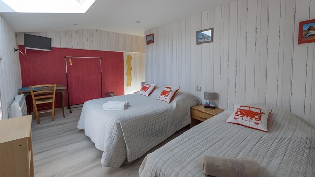 A room with two beds, a desk, a chair, and a TV mounted on the wall.