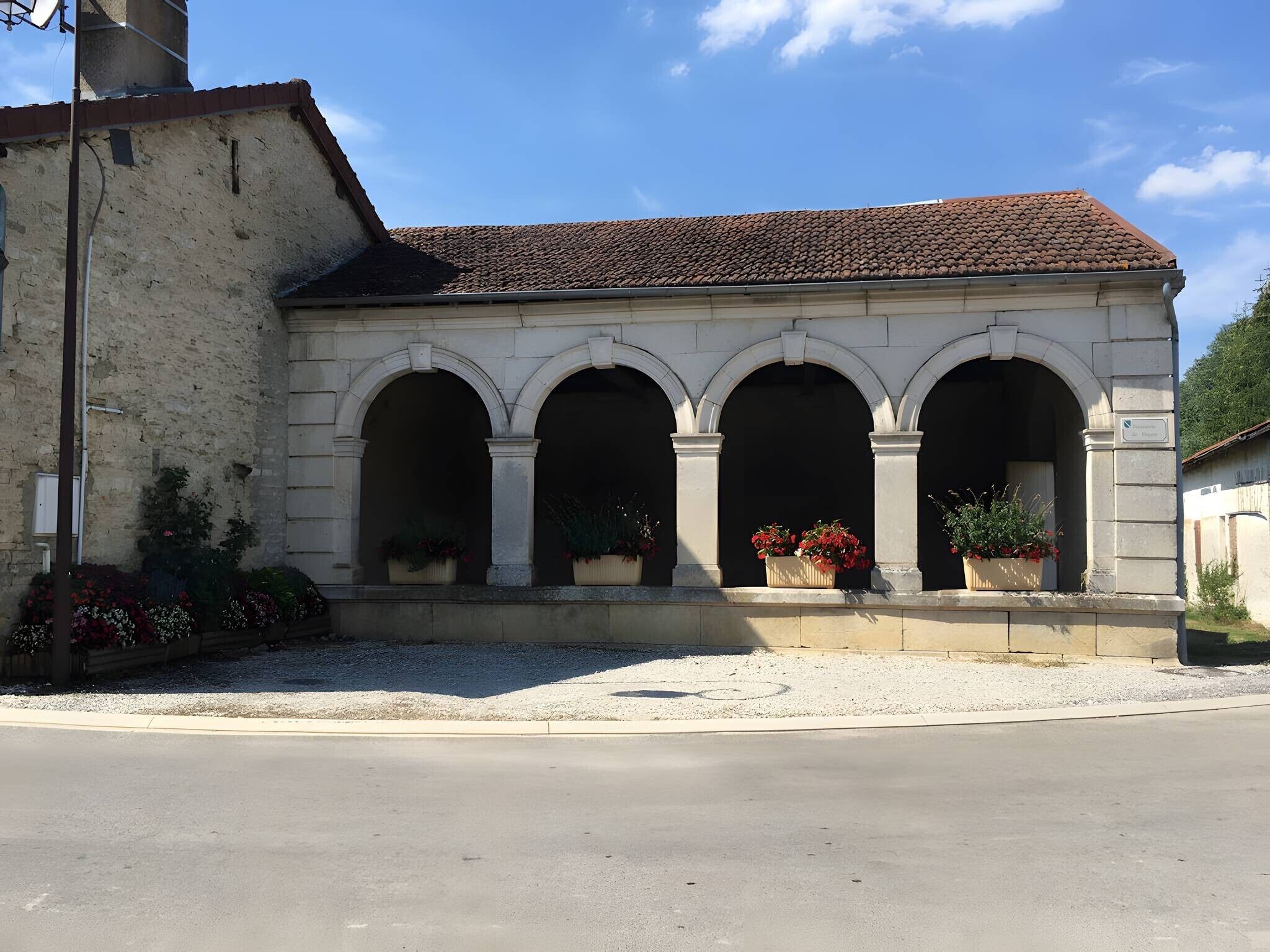 A building with a tiled roof, three arched windows, and flower pots on the ground level.