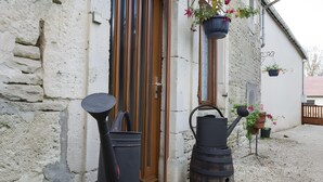A rustic building with a wooden door, a stone wall, and a gravel ground.