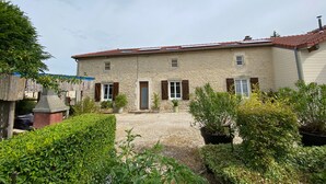A stone building with a tiled roof, a gravel driveway, and a variety of potted plants.