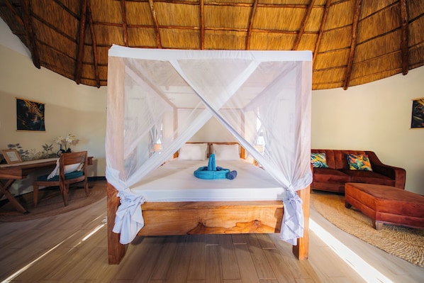 A bed with a canopy, wooden floor, and a thatched roof.