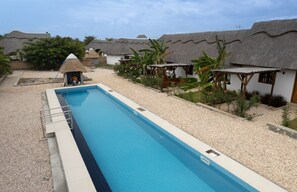 A swimming pool with a thatched-roof structure in the background.