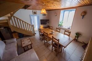 Un espace repas avec une table et des chaises en bois, un téléviseur fixé au mur et un escalier menant à un niveau supérieur.