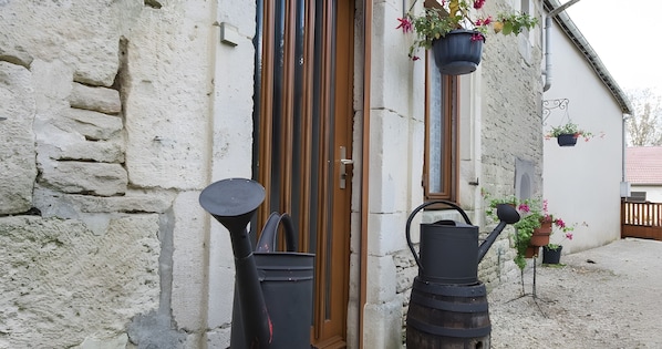 A rustic building with a wooden door, a stone wall, and a gravel ground.