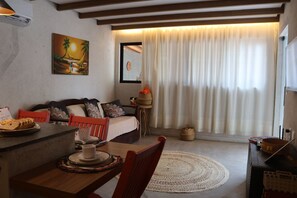 Ein gemütliches Wohnzimmer mit Essbereich, einem Gemälde an der Wand und einem großen Fenster mit Vorhängen.