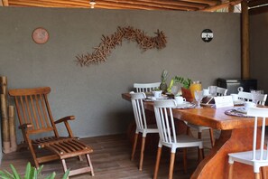 Ein Holztisch mit weißen Stühlen, einer Ananas und einem Glas Orangensaft.
