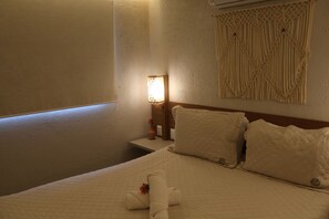 Ein Hotelzimmer mit einem Bett, einem Nachttisch, einer Wandlampe und einem dekorativen Wandbehang aus Makramee.