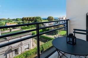 A balcony with a table and a lantern, overlooking a green landscape and buildings.