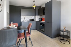 A compact kitchen with modern appliances, a dining area with a table and chairs, and a small side table with a candle holder.