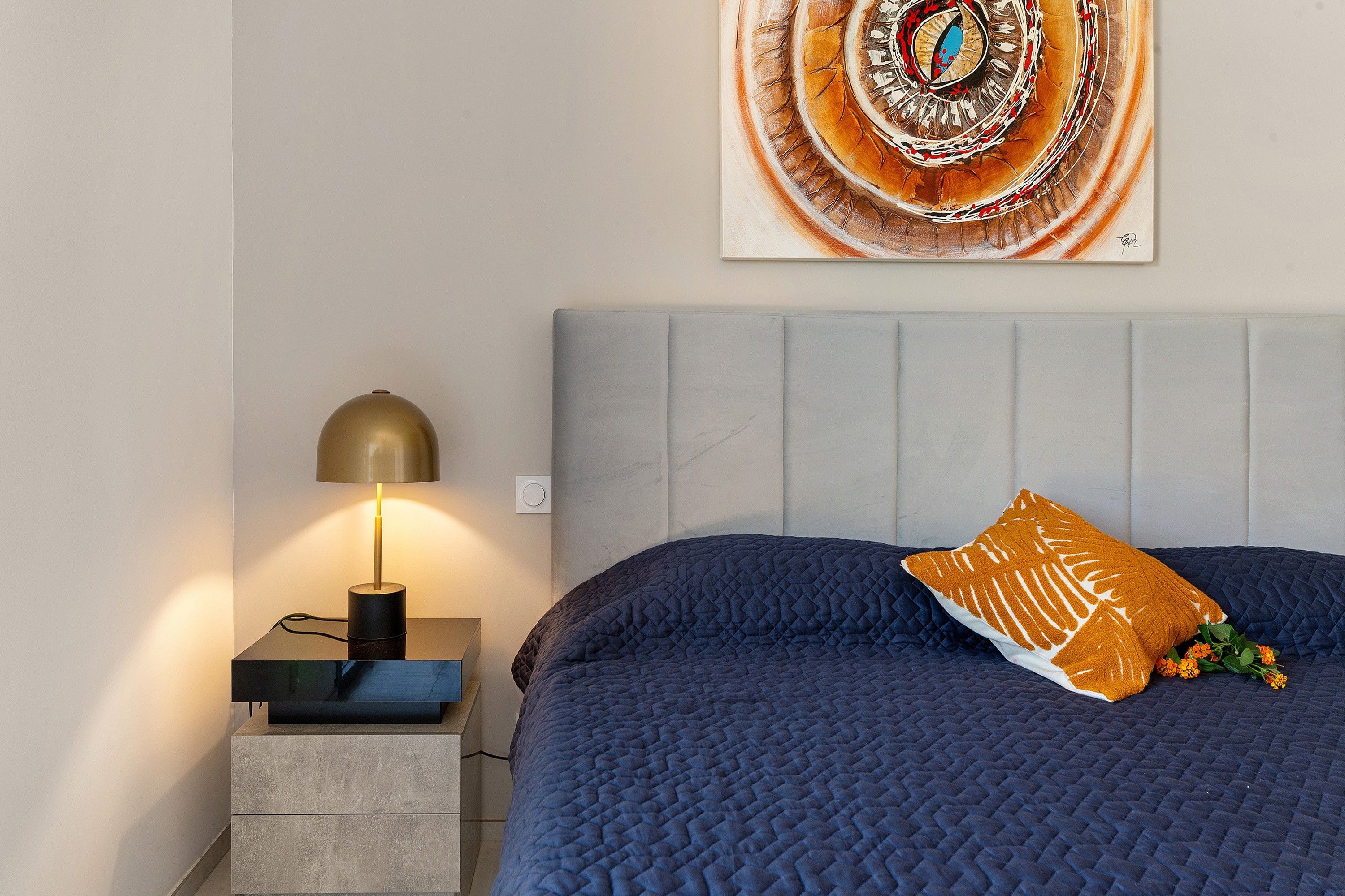 Ein Schlafzimmer mit einem Bett, einem Nachttisch mit Lampe und einem Wandbild.