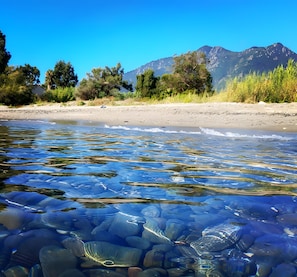 Une rivière aux eaux claires, avec des rochers et une plage de sable, des arbres et des montagnes en arrière-plan.