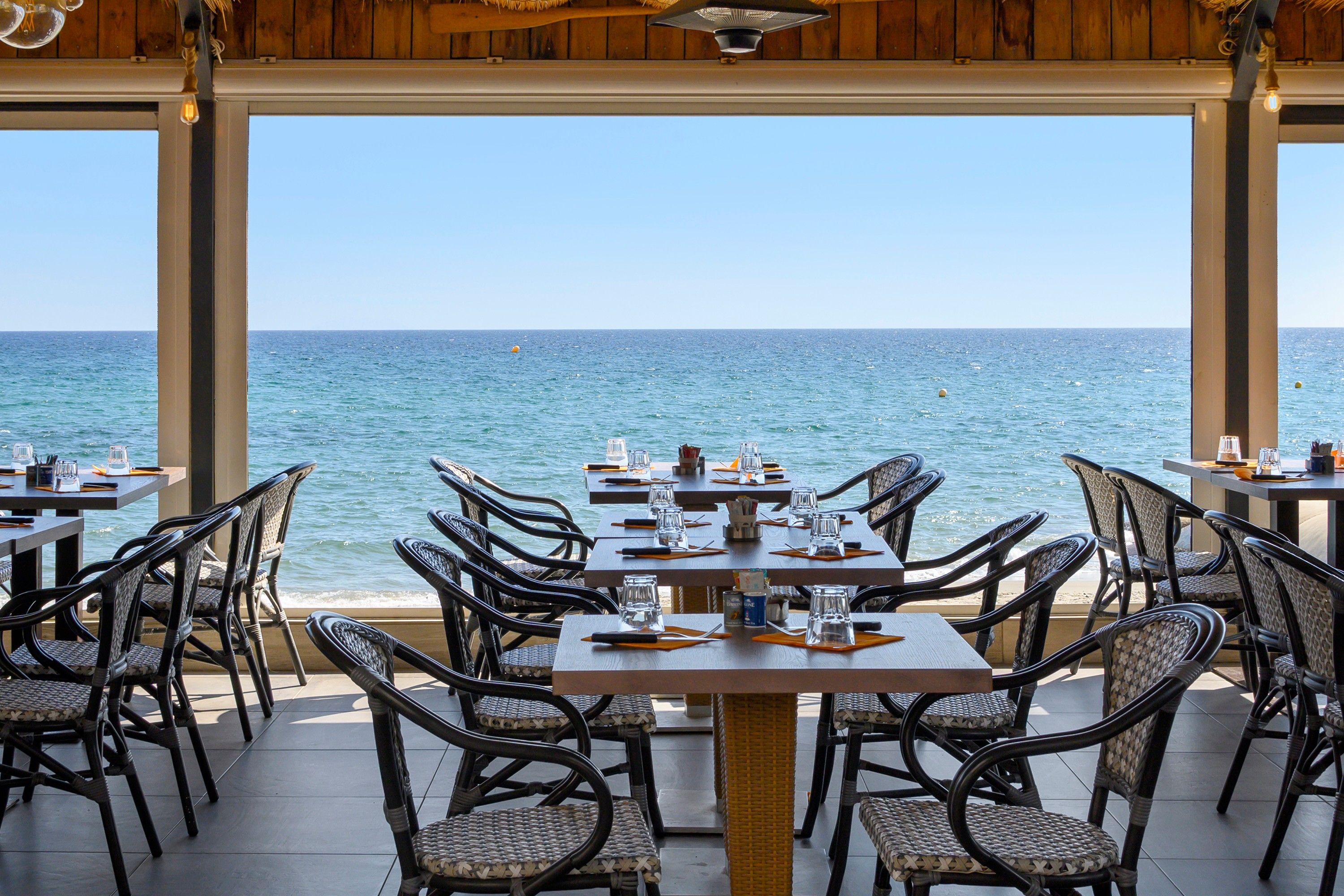 Een terras met tafels en stoelen met uitzicht op zee.