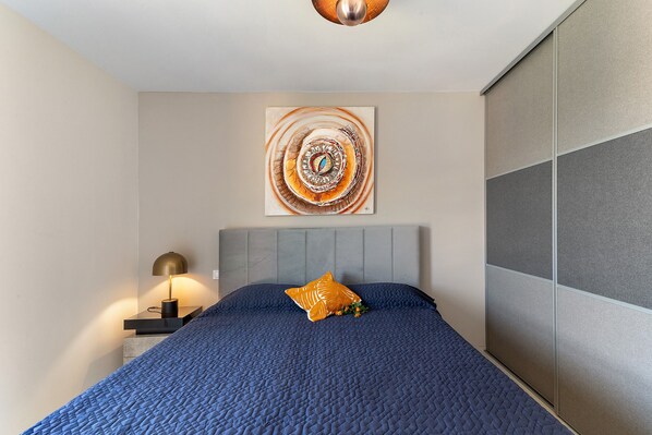 A bedroom with a bed, a nightstand, a lamp, and a wall-mounted artwork.