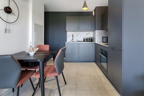 A modern kitchen with grey cabinets, a marble countertop, and a dining area with a table and chairs.